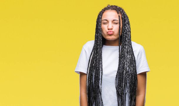Young braided hair african american girl over isolated background puffing cheeks with funny face. Mouth inflated with air, crazy expression. - Foto, imagen