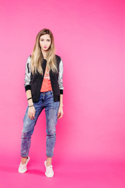 Девушка-подросток в джинсах и куртке позирует на фоне розовой студии
. - Фото, изображение