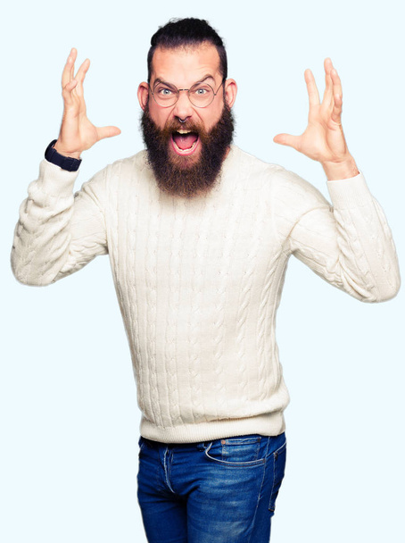 Young hipster man wearing glasses and winter sweater celebrating crazy and amazed for success with arms raised and open eyes screaming excited. Winner concept - Foto, afbeelding