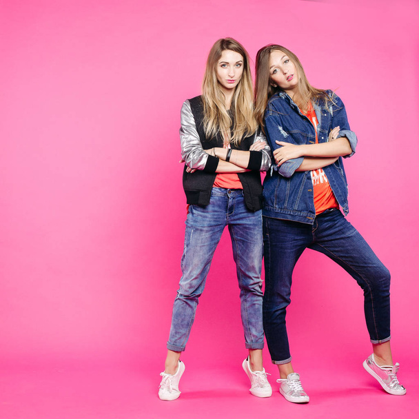 Δύο κομψά hipster στέκεται με σταυρωμένα χέρια και να ποζάρει στο ροζ studio. - Φωτογραφία, εικόνα