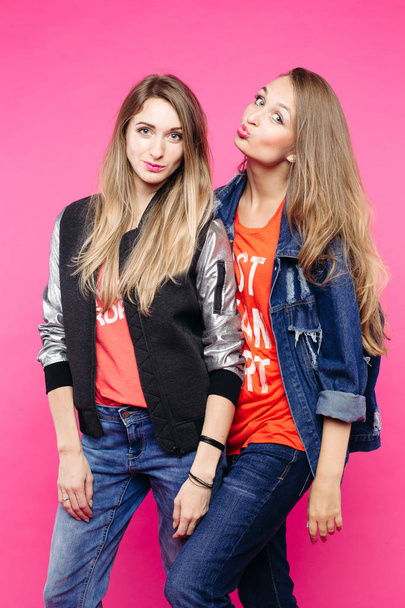Two girls having fun and posing at pink studio background. - Photo, Image