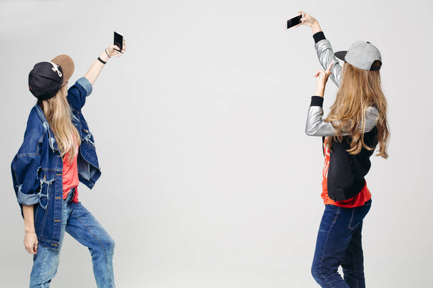 Kaksi tyttöä tyylikkäissä vaatteissa ottaen selfie älypuhelimeen
. - Valokuva, kuva