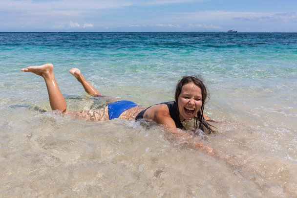 Καλοκαίρι lifestyle πορτρέτο της ευτυχής όμορφη νεαρή γυναίκα με σέξι μαυρισμένο σώμα. Απολαμβάνεις τη ζωή και ψέματα για τα καθαρά νερά της θάλασσας στην παραλία του τροπικού νησιού. Κομψή ευρεία Γείσο καπέλο. Πόδι επάνω - Φωτογραφία, εικόνα