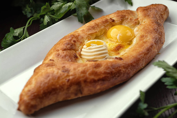 Adjar Khachapuri, an open pie with an egg, on a white plate. Traditional Georgian cuisine - Photo, Image