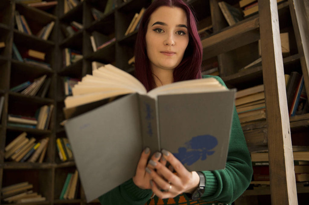  una bella ragazza con un libro aperto su uno sfondo sfocato di scaffali con libri
 - Foto, immagini
