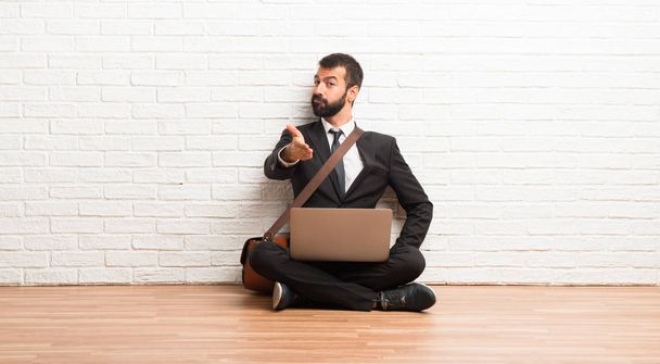 Бизнесмен с ноутбуком сидит на полу и пожимает руку после выгодной сделки.
 - Фото, изображение