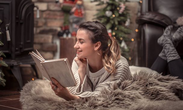 girl reading a book in a cozy home atmosphere near the fireplace, the concept of home rest - Foto, Imagen