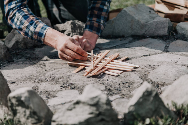 fire in the fire. A hand in a blue checkered shirt fires the fire with matches on a stone campfir - Fotoğraf, Görsel