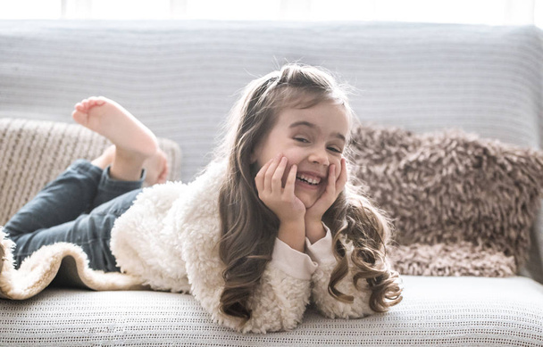 glückliches kleines Mädchen auf der Couch liegend, schönes Lächeln, Ruhekonzept - Foto, Bild