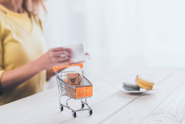 selective focus of small paper boxes in toy shopping trolley with woman on background - Фото, зображення
