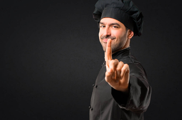 Chef man In black uniform showing and lifting a finger in sign of the best on black background - Photo, Image