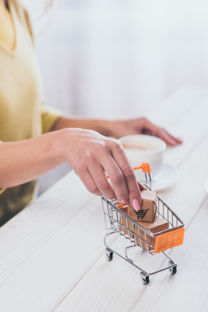 selective focus of woman putting toy paper box in small shopping trolley with cup on background - Fotografie, Obrázek