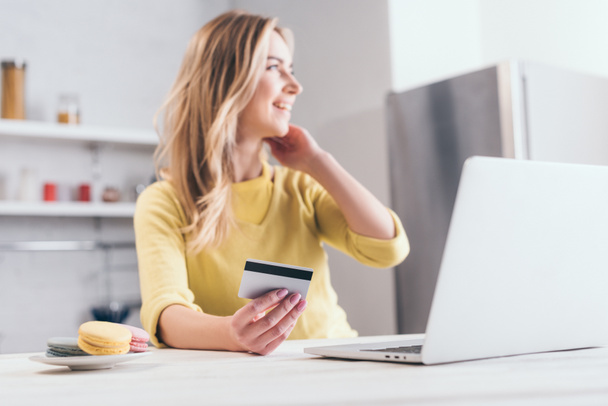 Selektivní fokus z kreditní karty v ruce blond žena poblíž laptop  - Fotografie, Obrázek