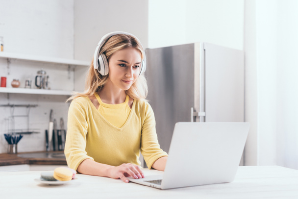 ελκυστική ξανθιά γυναίκα ακούγοντας μουσική στα ακουστικά κατά τη χρήση του φορητού υπολογιστή - Φωτογραφία, εικόνα
