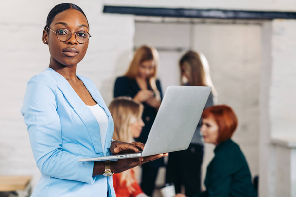 business black woman adjusting laptop, standing with office colleagues behind - 写真・画像