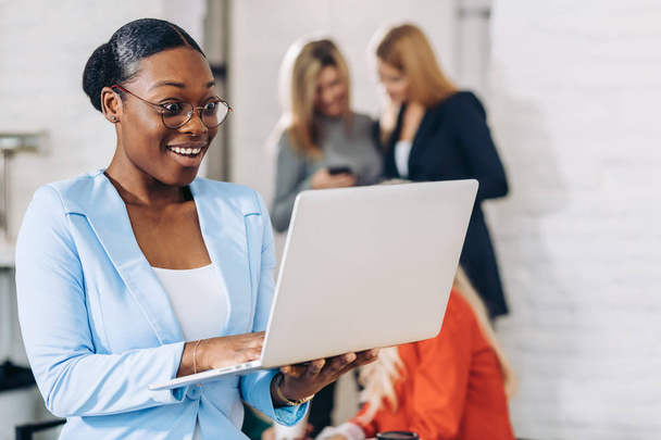 business zwart vrouw aanpassen laptop, staan met office collega 's achter - Foto, afbeelding