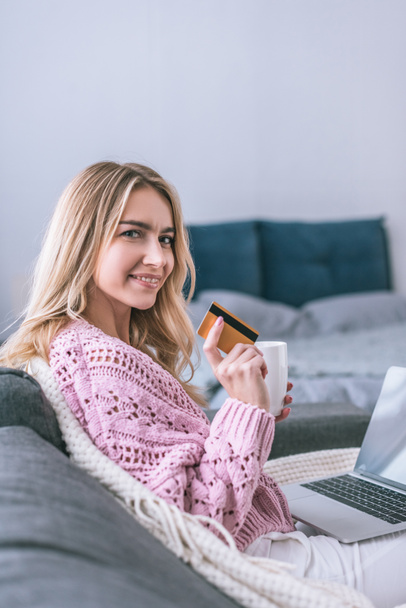 attractive woman smiling and holding credit card and cup in hands  - Foto, Bild