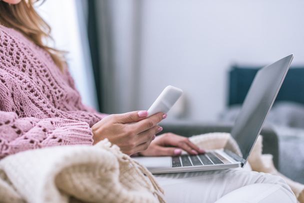 cropped view of female blogger using laptop and holding smartphone at home  - Foto, Imagem