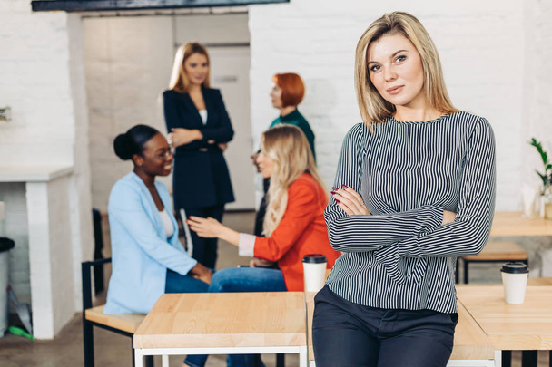 Blonde business woman smiles at camera with colleagues working in background - Foto, imagen