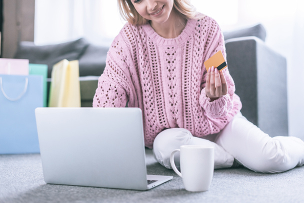 cropped view of cheerful woman holding credit card and sitting near laptop - 写真・画像