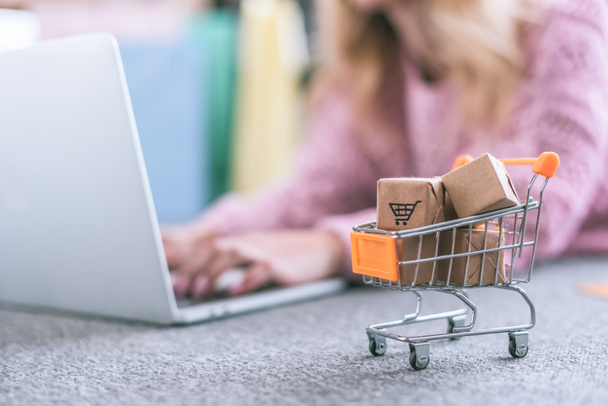 selective focus of small cart with toy paper boxes with woman using laptop on background - Foto, Bild