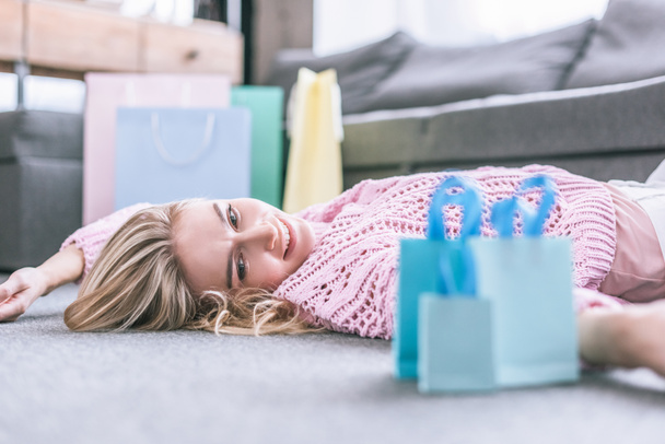 cheerful woman looking at shopping bags while lying in floor at home - Foto, Imagem