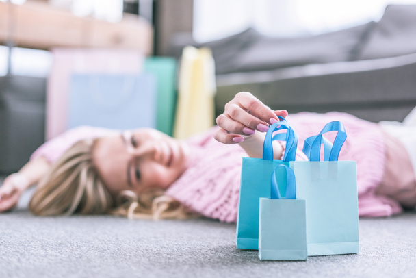 selective focus of shopping bags with happy woman lying on floor on background - Fotoğraf, Görsel