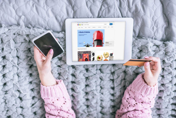 περικοπεί προβολή της γυναίκας κρατώντας πιστωτική κάρτα και το smartphone κοντά στο ψηφιακό tablet με το ebay app στην οθόνη - Φωτογραφία, εικόνα