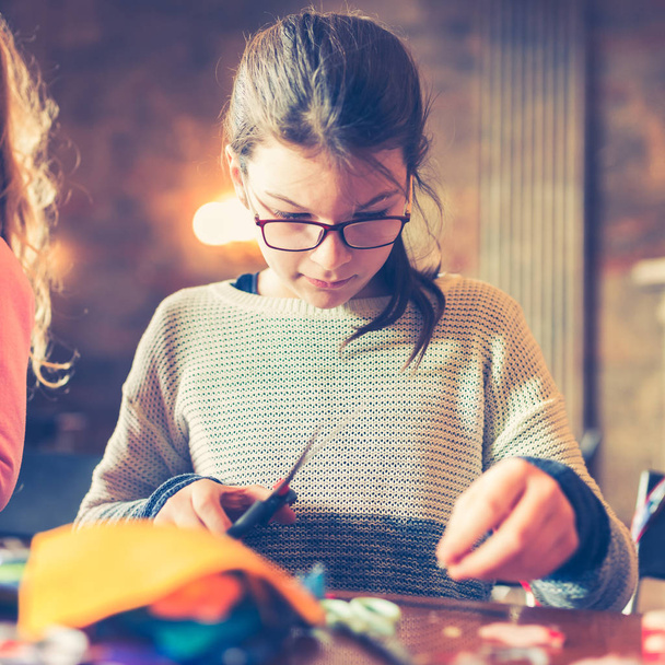 oficinas de arte de alfaiate de crianças - uma menina que cose decorações sentidas - tecidos coloridos que se encontram em uma mesa
 - Foto, Imagem