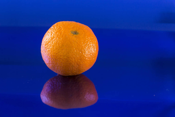 una mandarina solitaria sobre un fondo azul metálico con reflejos
 - Foto, Imagen