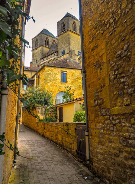 Callejón estrecho y pintoresco con casas antiguas que conducen a la iglesia de San Pedro en el centro del pueblo medieval de Gourdon, Lot, Francia
 - Foto, imagen