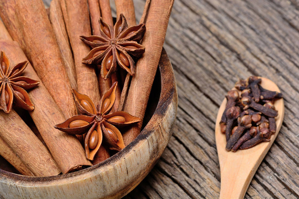 Cinnamon sticks with star anise in a bowl and cloves in a wooden spoon on table - Photo, Image