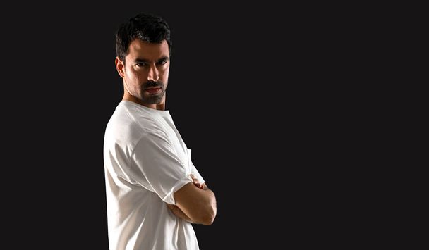 Young man with white shirt with his arms crossed on isolated black background - Photo, image