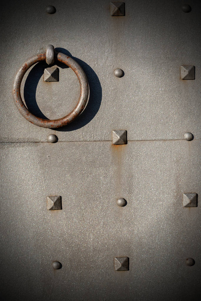 Fondo metálico - Detalle de una vieja puerta metálica con pernos en forma de pirámide y forma de anillo de mango
 - Foto, imagen