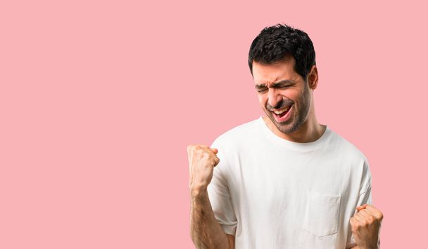 Young man with white shirt celebrating a victory and happy for having won a prize on isolated pink background - Foto, Imagem