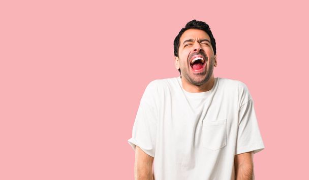 Hombre joven con camisa blanca gritando al frente con la boca abierta sobre fondo rosa aislado
 - Foto, imagen