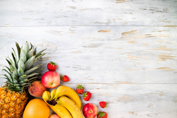 Frutas frescas na velha mesa de madeira. Abacaxi, banana, maçã, morango, citrinos e pêssego. Alimentação saudável, dieta, conceito de alimentação limpa. Vista superior, espaço de cópia
 - Foto, Imagem