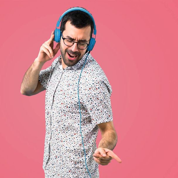 Handsome man with glasses listening music on pink background - Foto, afbeelding