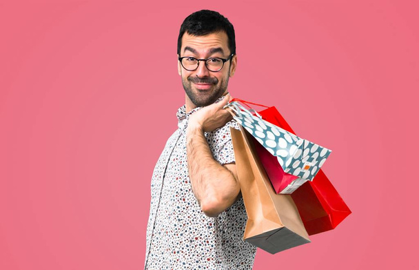 ピンクの背景のショッピング バッグとメガネがハンサムな男 - 写真・画像