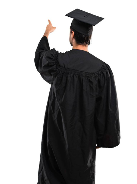 Man on his graduation day University pointing back with the index finger on isolated white background - Photo, Image
