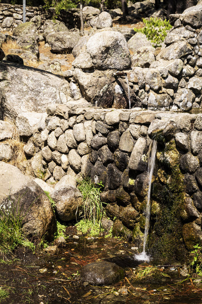 струмінь прісної води, що виходить з металевого носика з кам'яного фонтану в горі
 - Фото, зображення