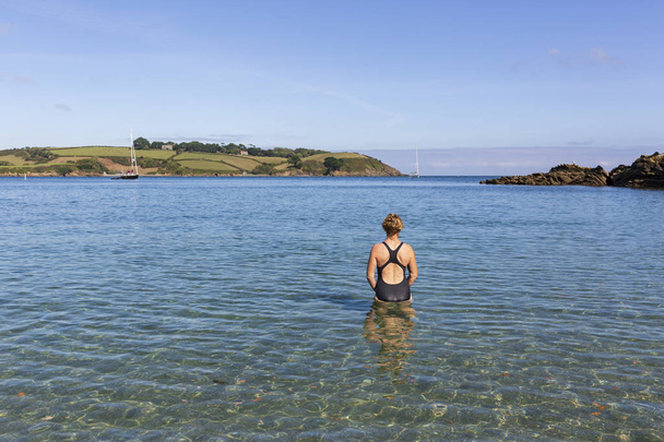 Woman wearing a swimming costume entering the cool, clear water at Bosahan Cove on the the Helford River Estuary in Cornwall, England. - Photo, Image