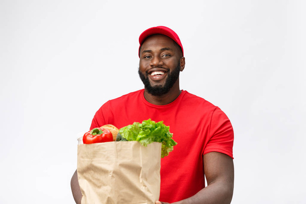 Teslimat Konsepti - Yakışıklı Afro-Amerikalı teslimatçı marketten paket yiyecek ve içecek taşıyor. Grey Stüdyo Arkaplanı 'nda izole edilmiş. Boşluğu Kopyala - Fotoğraf, Görsel