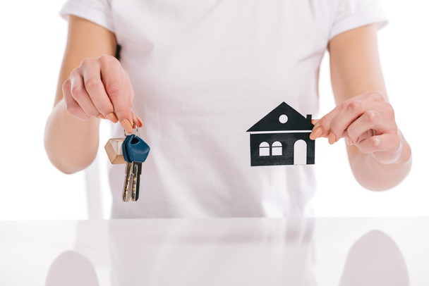 частичный взгляд женщины, держащей бумажный дом и ключи, изолированные на белом, ипотечная концепция
 - Фото, изображение