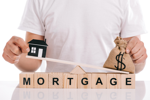 partial view of man holding moneybag and paper house on scales on cubes with mortgage lettering isolated on white - Photo, Image
