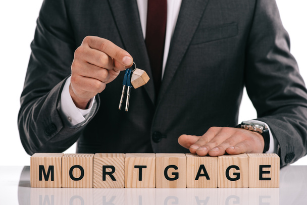 cropped view of businessman holding keys near wooden cubes with mortgage lettering isolated on white - Photo, Image