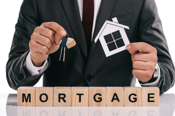 cropped view of mortgage broker holding paper house and keys near wooden blocks isolated on white - Photo, Image