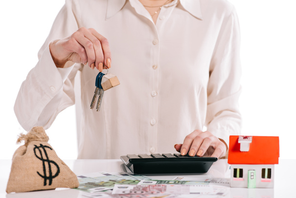 cropped view of businesswoman holding keys and using calculator isolated on white, mortgage concept - Photo, Image
