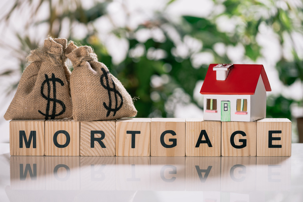 selective focus of moneybags with dollar signs and house model on wooden cubes with letters, mortgage concept - Photo, Image