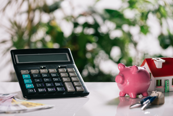 selective focus of euro banknotes, keys, piggy bank, calculator and house model on white desk, mortgage concept - Photo, Image